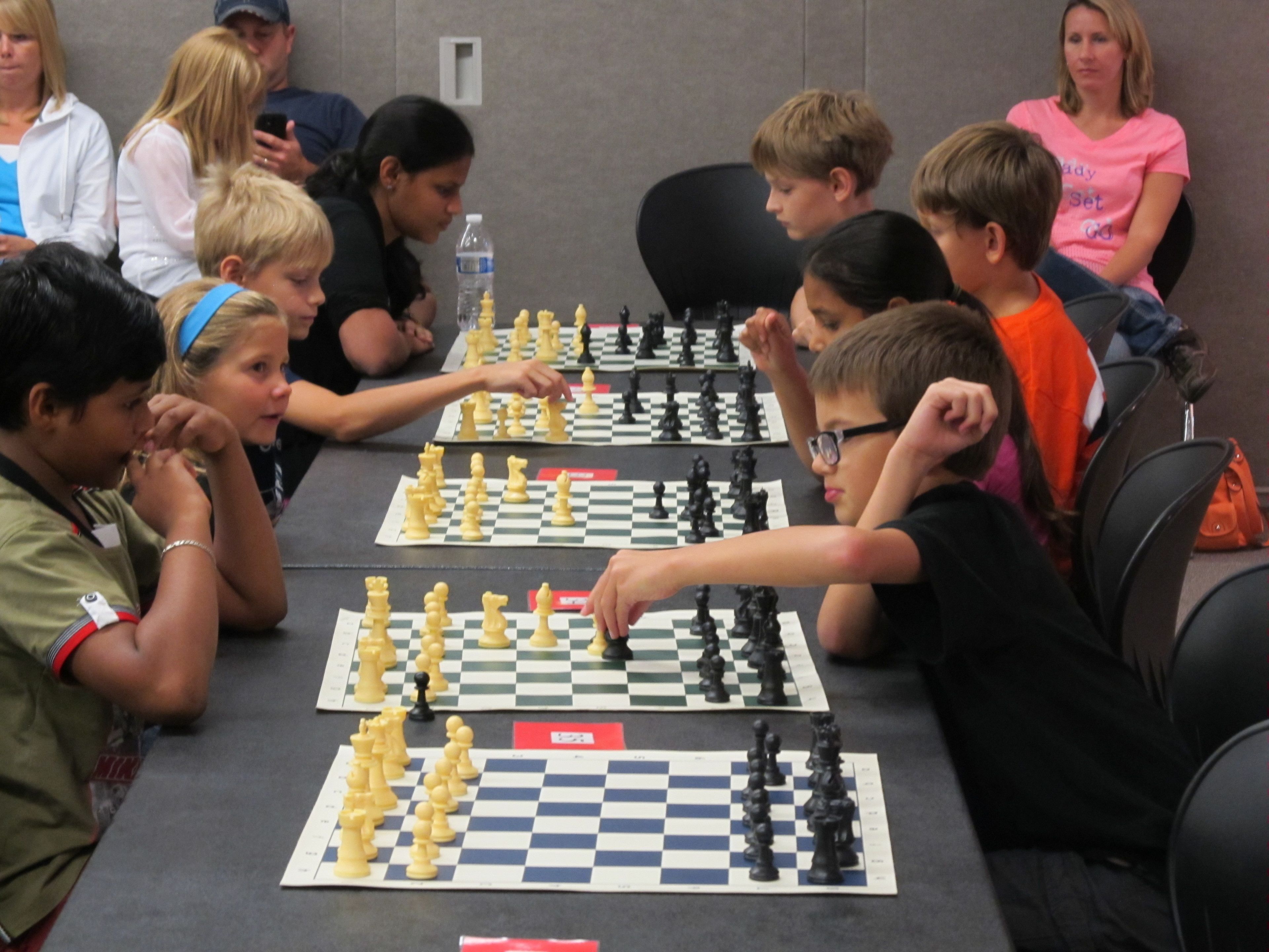 A group of people playing chess at a table with a water bottle on it.