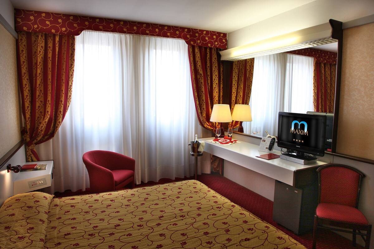 Ein Hotelzimmer mit einem Bett, zwei roten Sesseln, einem Schreibtisch mit Fernseher und einer Minibar.