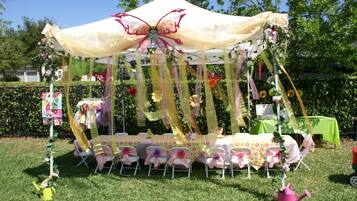 A tent with a floral canopy, surrounded by tables and chairs, set up on a grassy area.