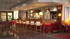 Vestíbulo de hotel con zona de bar, asientos y un letrero de 'MAXIM' en el suelo.