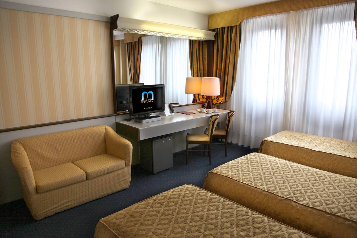 Ein Hotelzimmer mit Sofa, Schreibtisch mit Computer, Fernseher und zwei Betten.