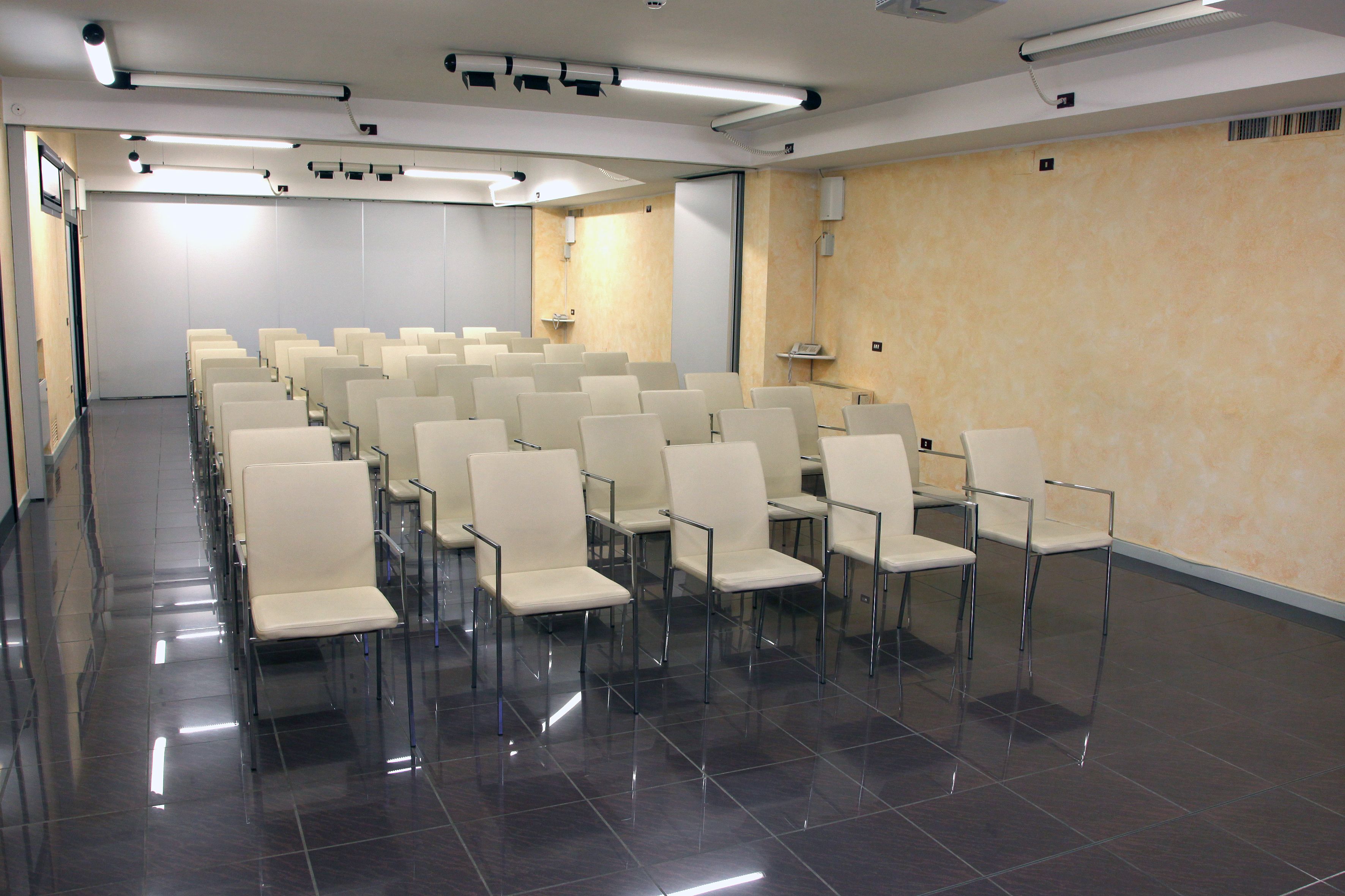 A conference room with rows of white chairs, a projector, and a screen.