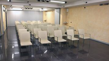 A conference room with rows of white chairs, a projector, and a screen.