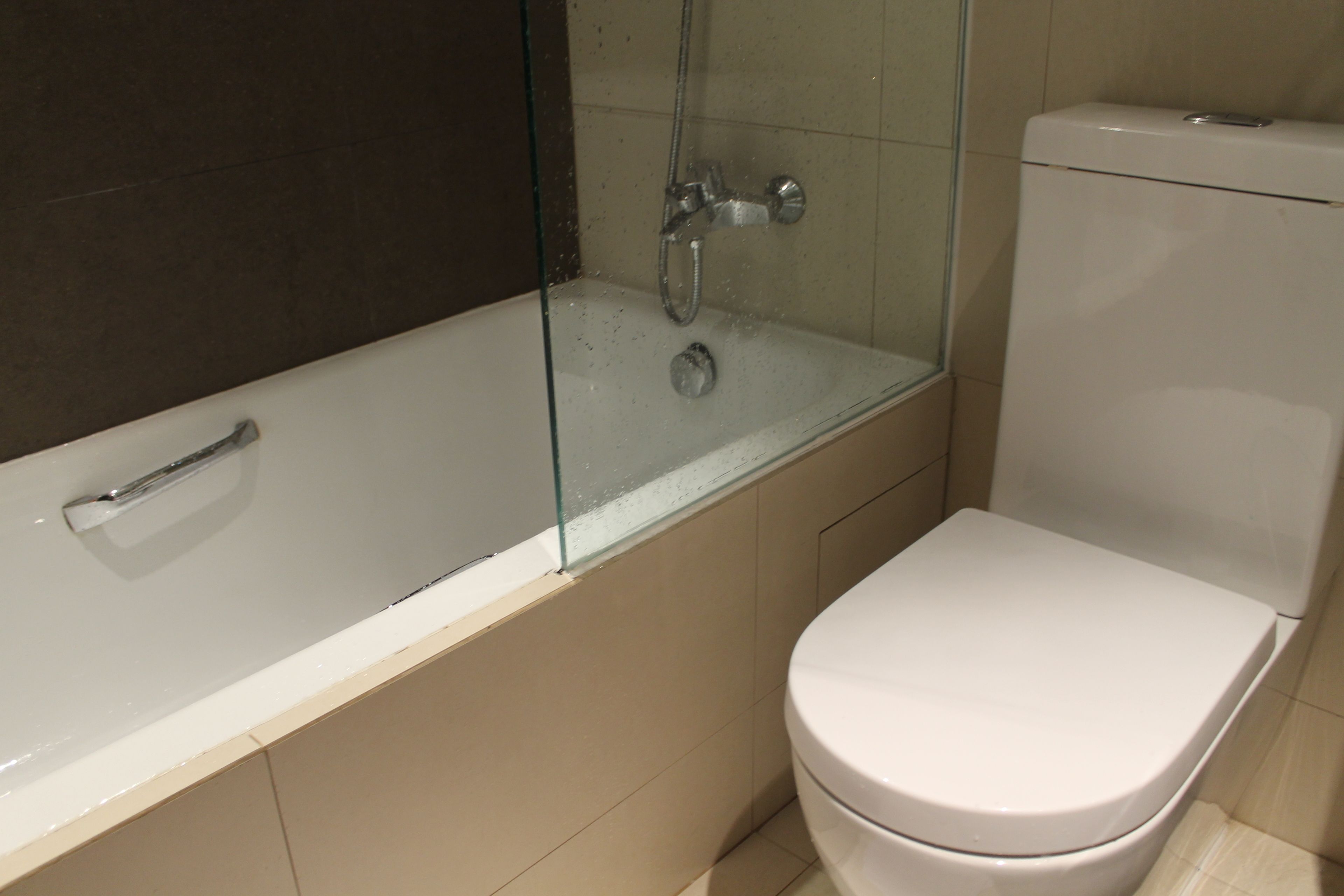 Ein Badezimmer mit einer in Glas abgeschirmten Dusche, einer weißen Badewanne und einem weißen WC.