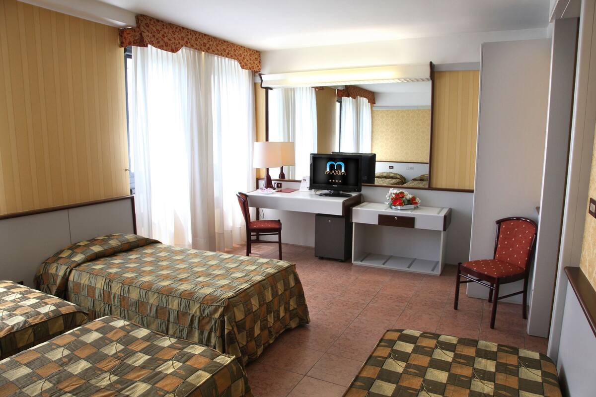 Ein Hotelzimmer mit zwei Betten, einem Schreibtisch, einem Fernseher, einem Sessel und einem Spiegel.