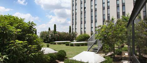 A modern building with a courtyard featuring stone pathways, neatly trimmed hedges, and a staircase leading to an upper level.