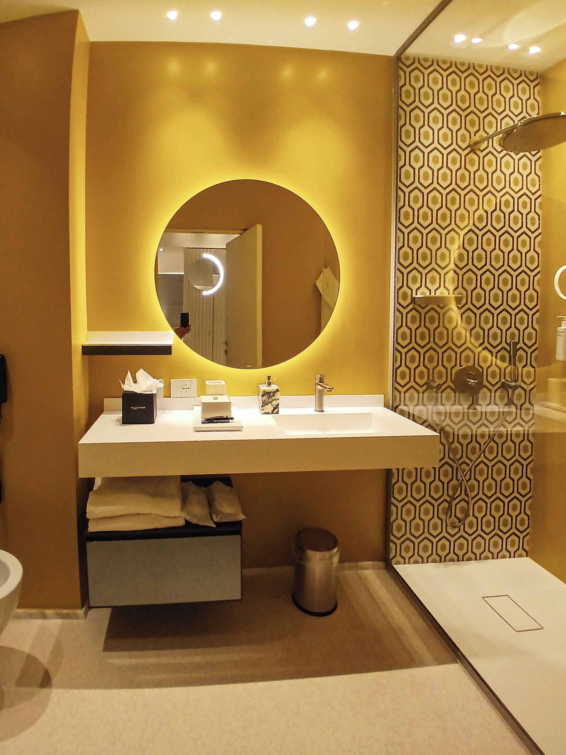 A modern bathroom with a round mirror, a white sink, and a patterned wall.