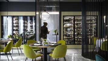 A modern restaurant interior with a wine cellar, green chairs, and a person reading a menu.
