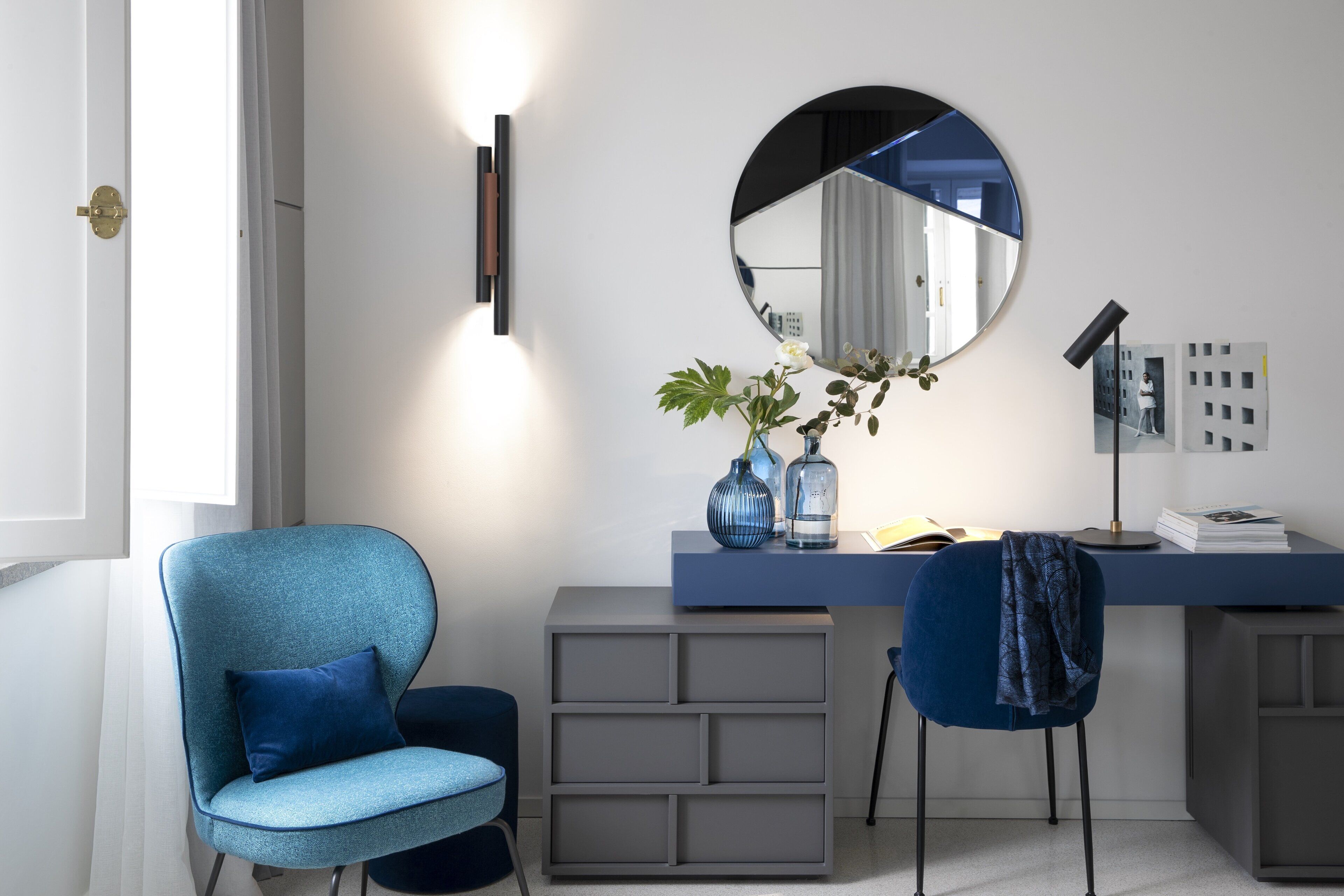 A modern room with a desk, two chairs, a large mirror, and a bookshelf.