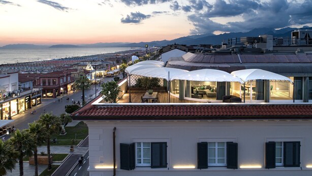 A coastal hotel with a terrace overlooking the beach, a dining area with umbrellas, and a view of the sea and mountains. - Hotel Plaza e de Russie (Viareggio)