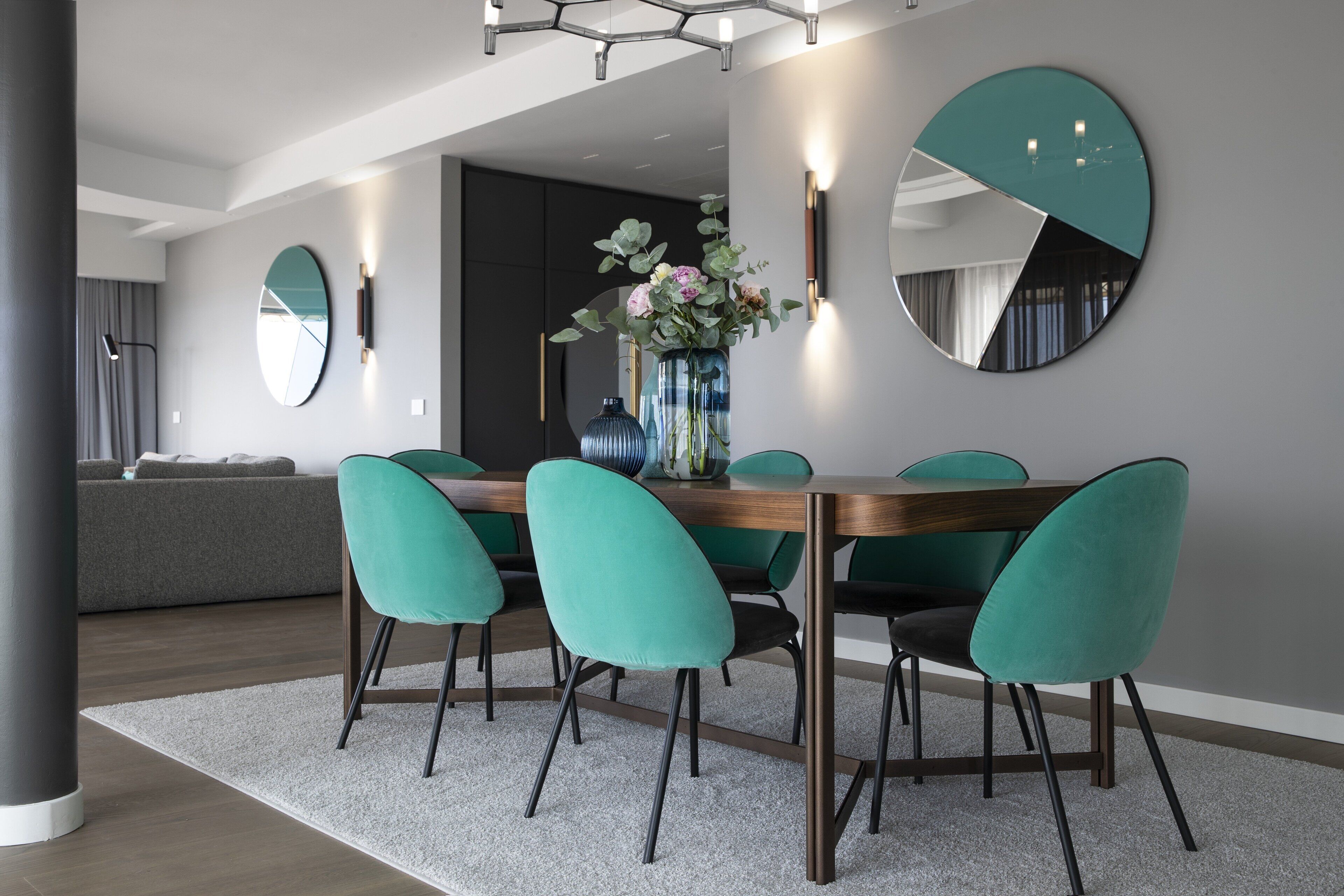 A modern dining area with a round table, teal chairs, and a vase of flowers.