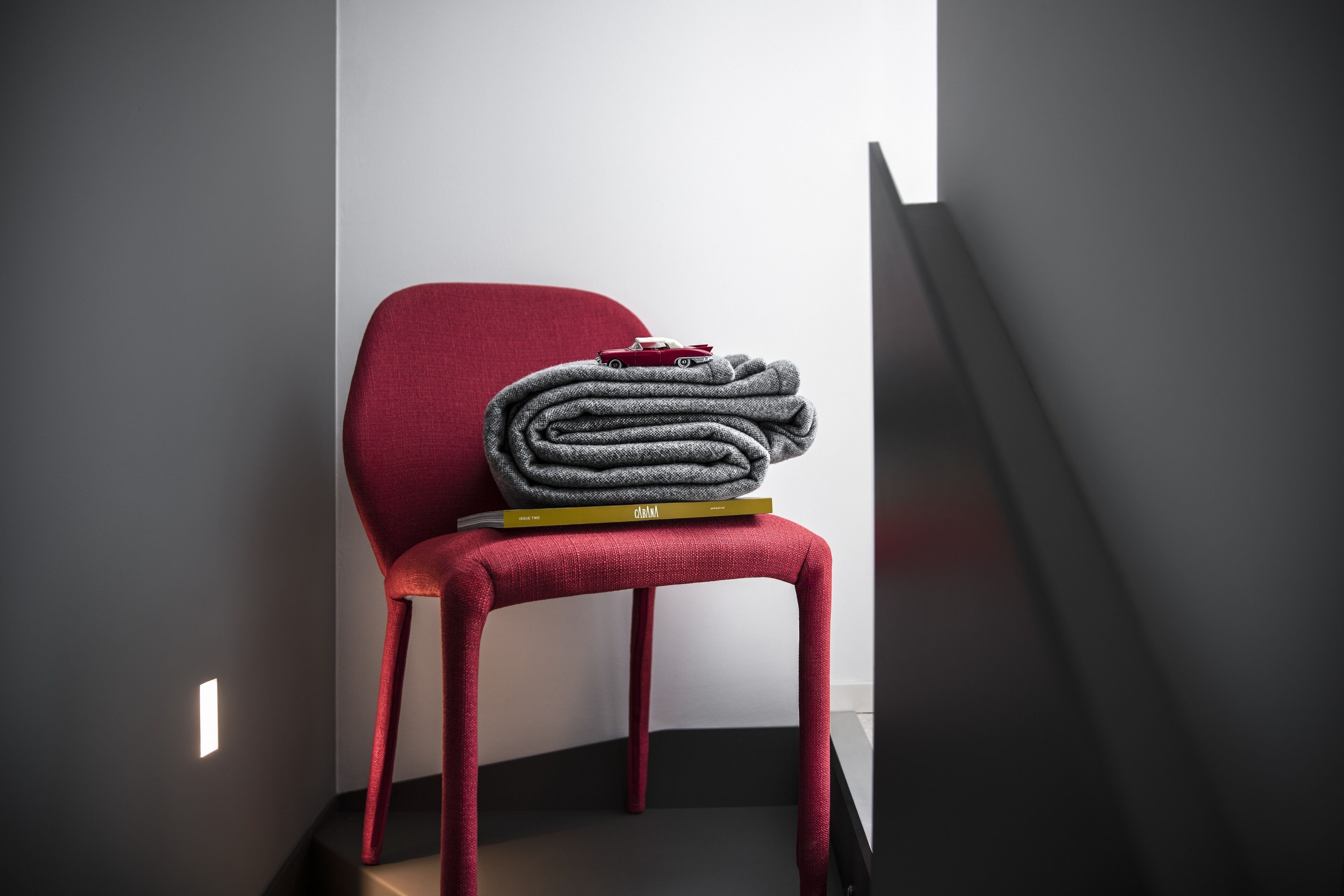 Ein moderner Stuhl mit roter Rückenlehne und einer grauen Decke darauf.