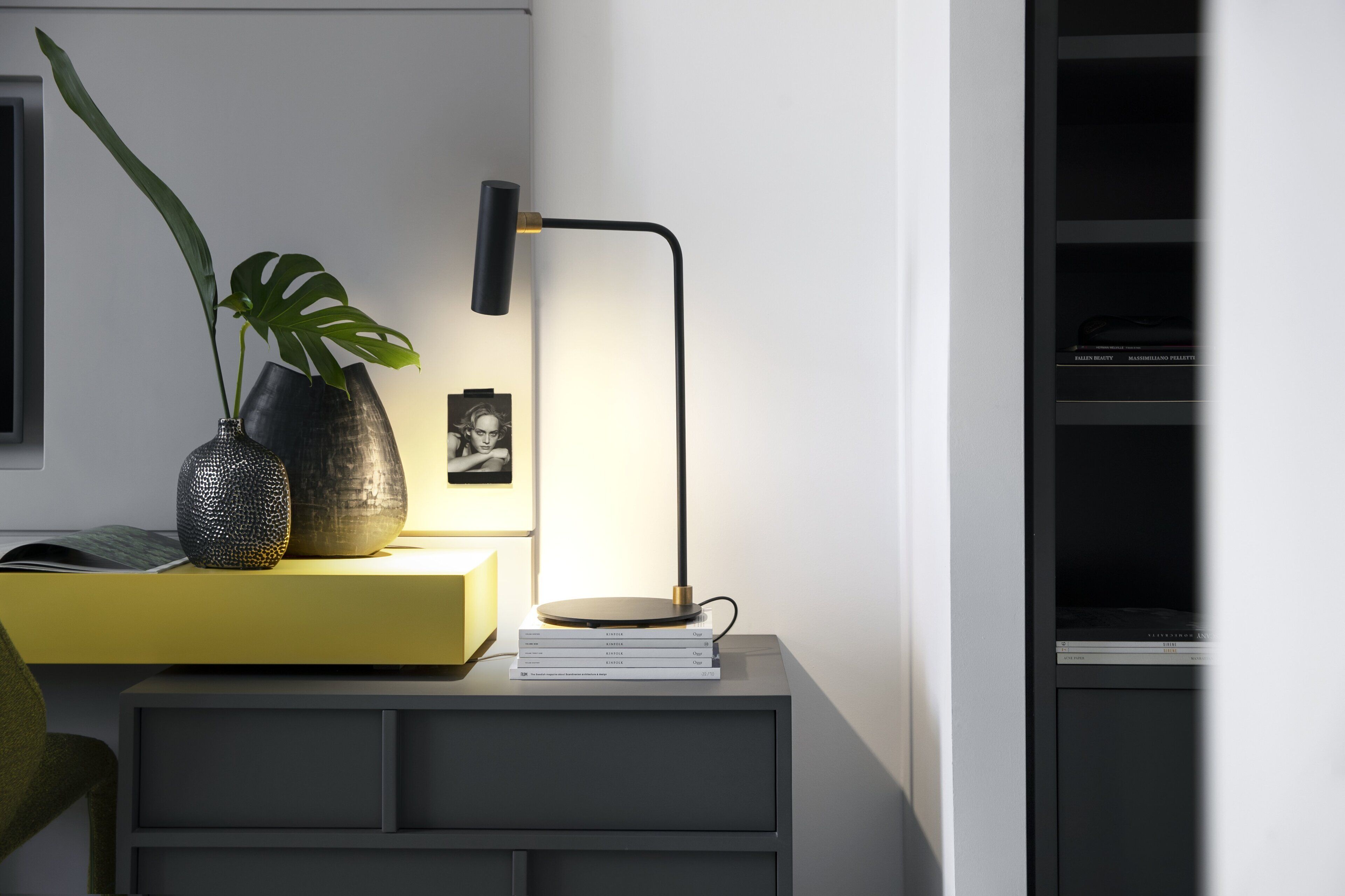 A bedside table with a lamp, a potted plant, and books.