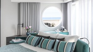A modern hotel room with a large bed, a round mirror, a view of the sea, and a nightstand with a lamp and a vase of flowers. - Hotel Plaza e de Russie (Viareggio)