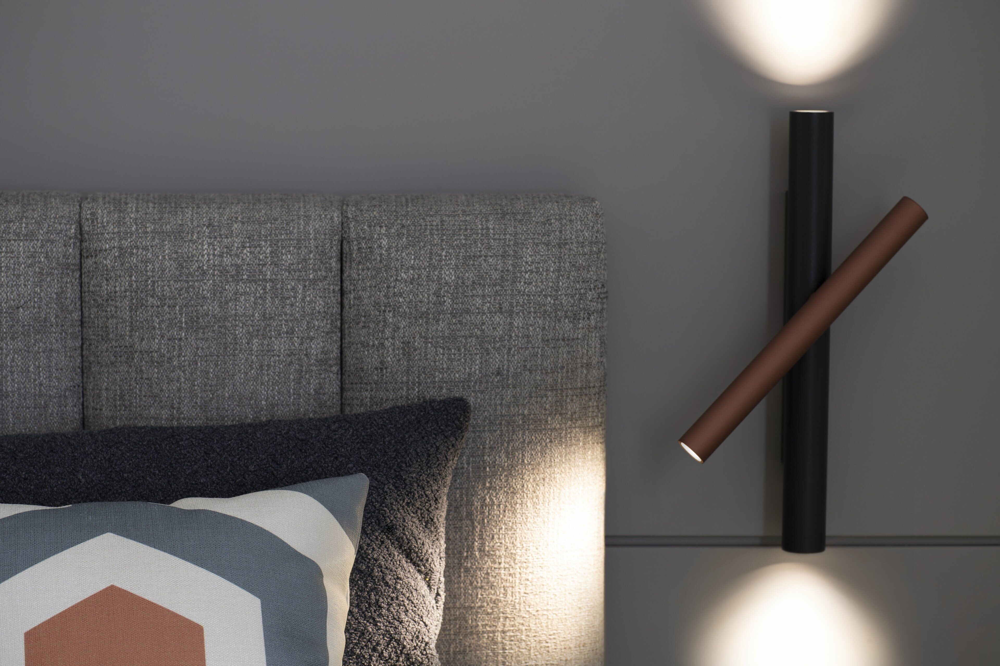 Une pièce moderne avec un canapé gris, un coussin à motifs géométriques et un luminaire fixé au mur.