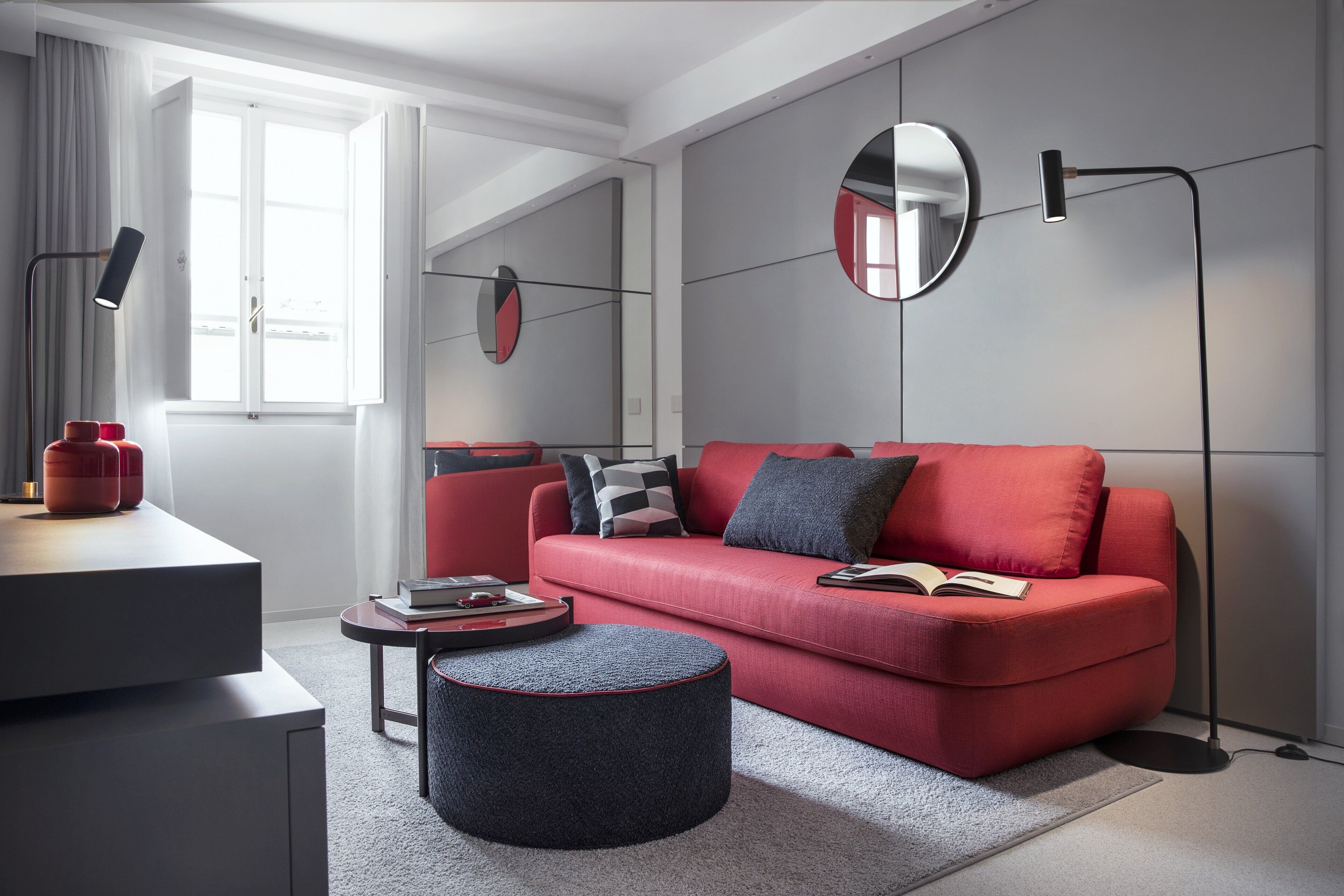 A modern living room with a red sofa, a round ottoman, a side table with books, and a floor lamp.