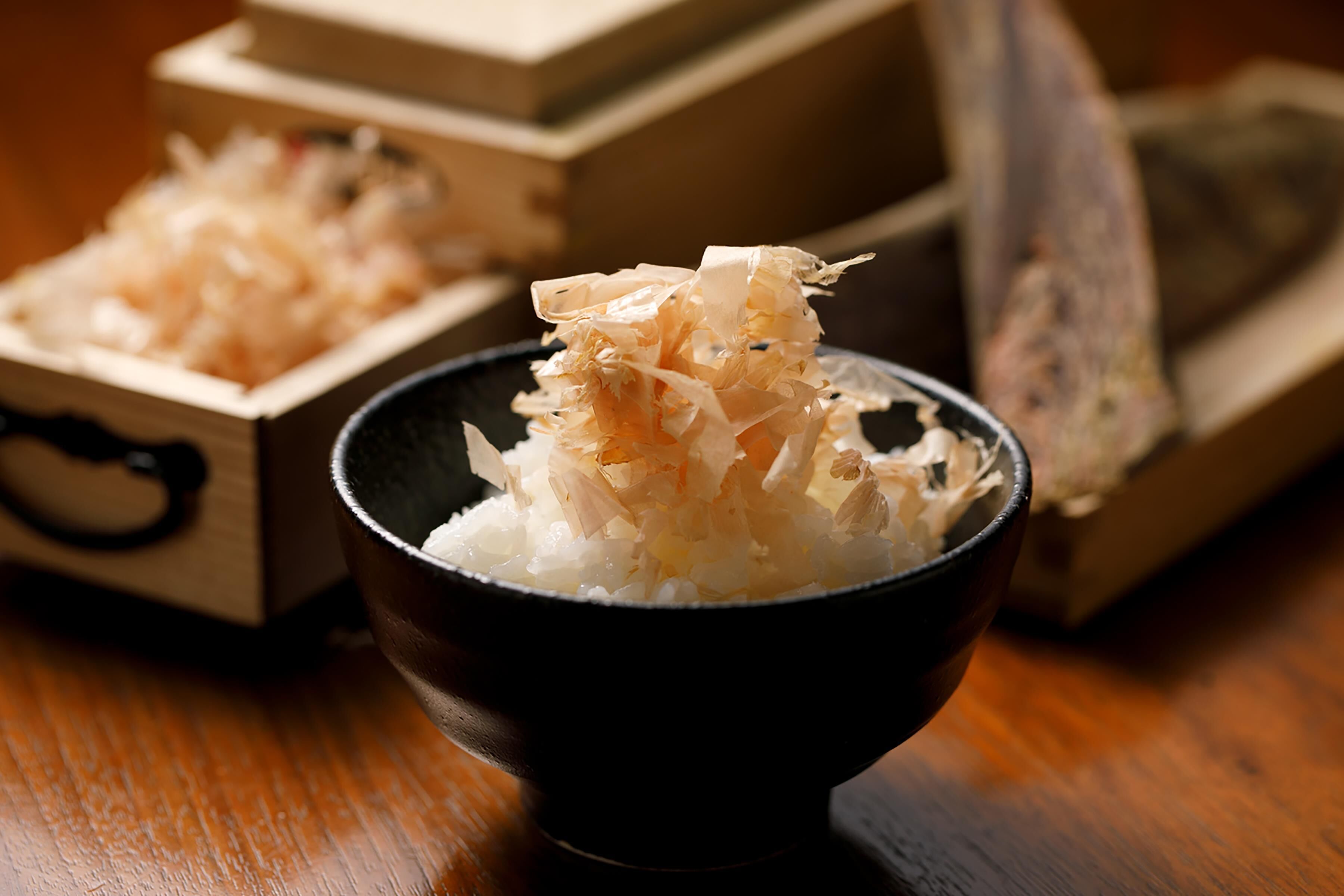 A bowl of rice topped with shredded seaweed, with wooden boxes and a piece of wood in the background.