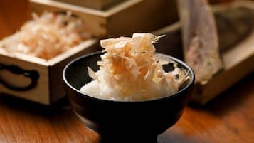 A bowl of rice topped with shredded seaweed, with wooden boxes and a piece of wood in the background.