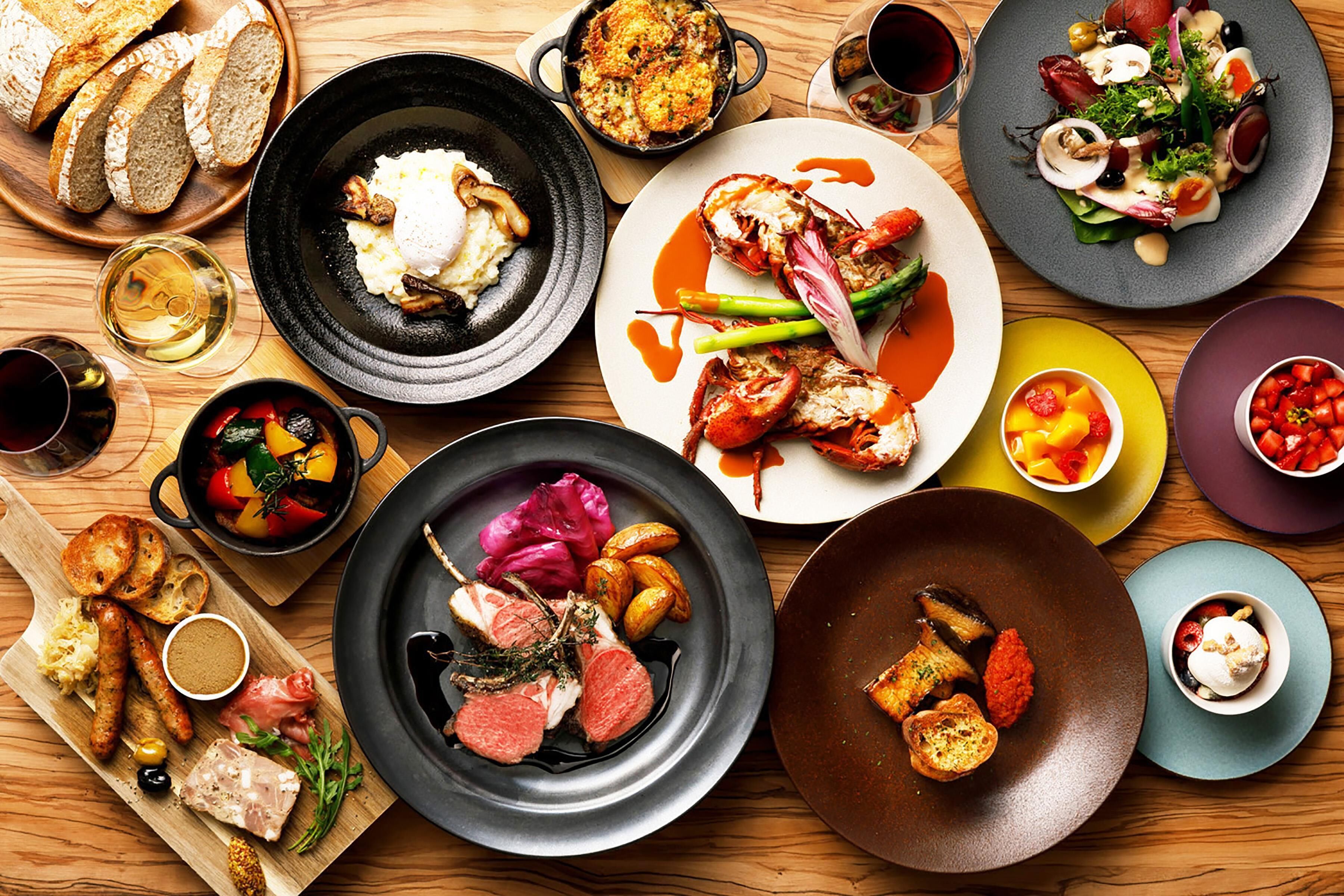 A variety of dishes on a wooden table, including bread, roasted vegetables, and seafood.