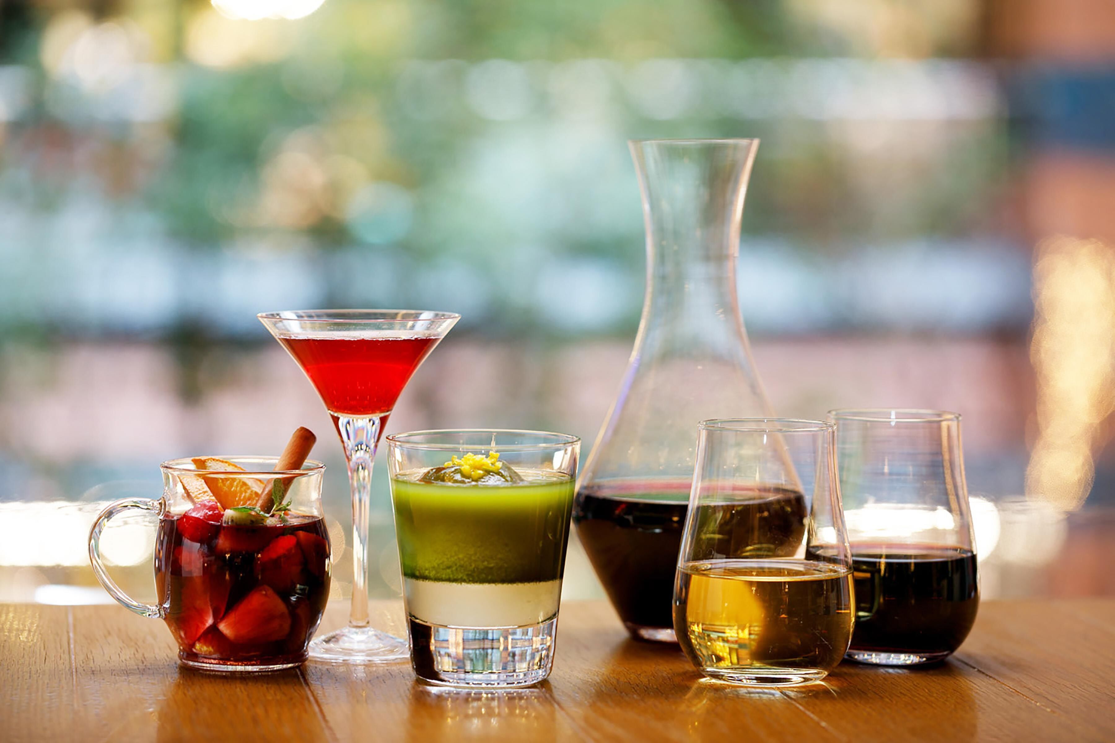 A variety of drinks on a wooden table, including a pitcher, a martini glass, and several shot glasses.