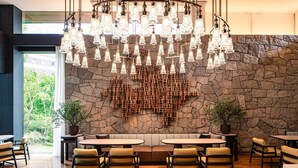 Een modern restaurantinterieur met een stenen muur, houten zitplaatsen en een unieke verlichtingsarmatuur.