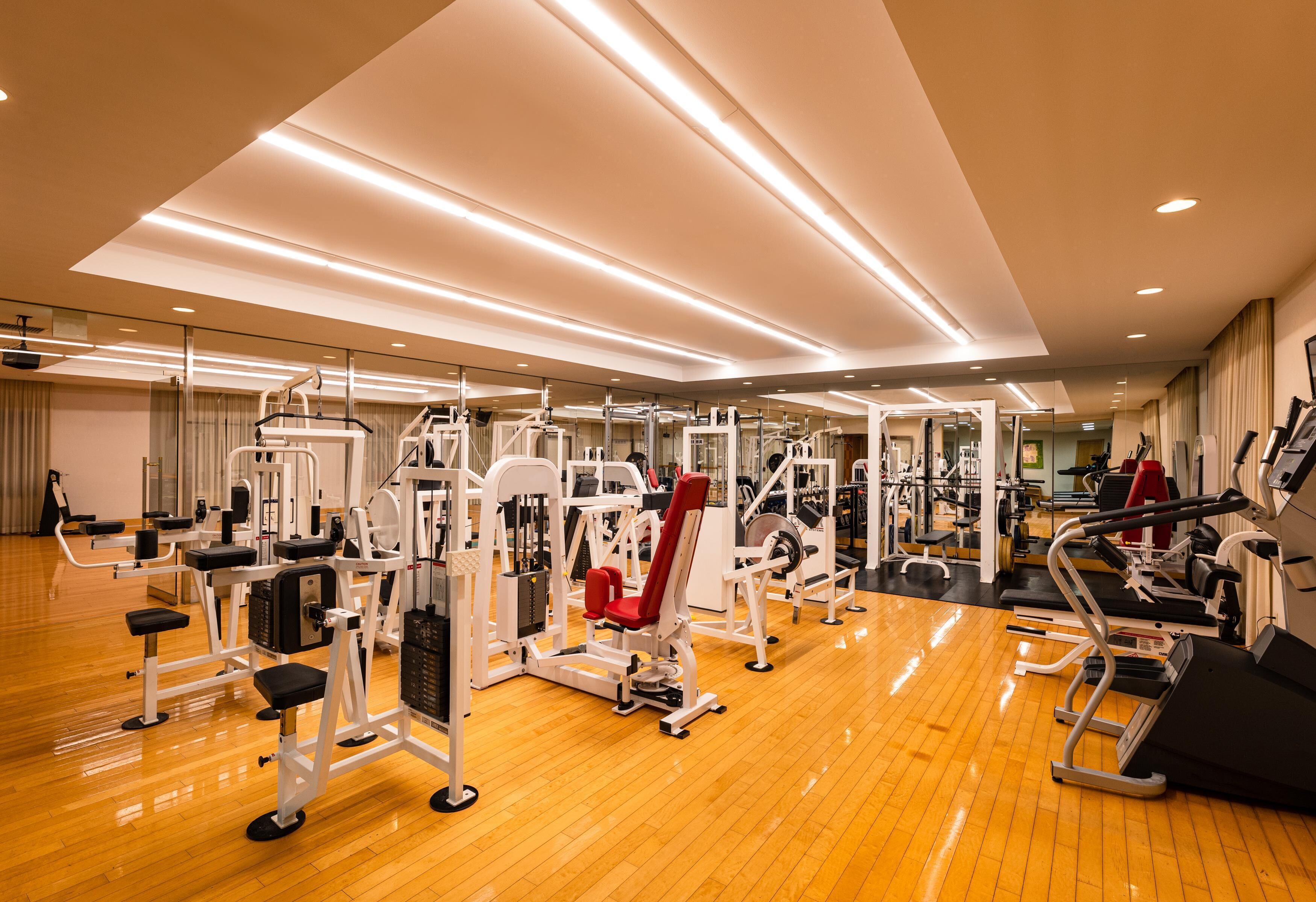 A spacious gym with various exercise machines, a wooden floor, and a large mirror wall.