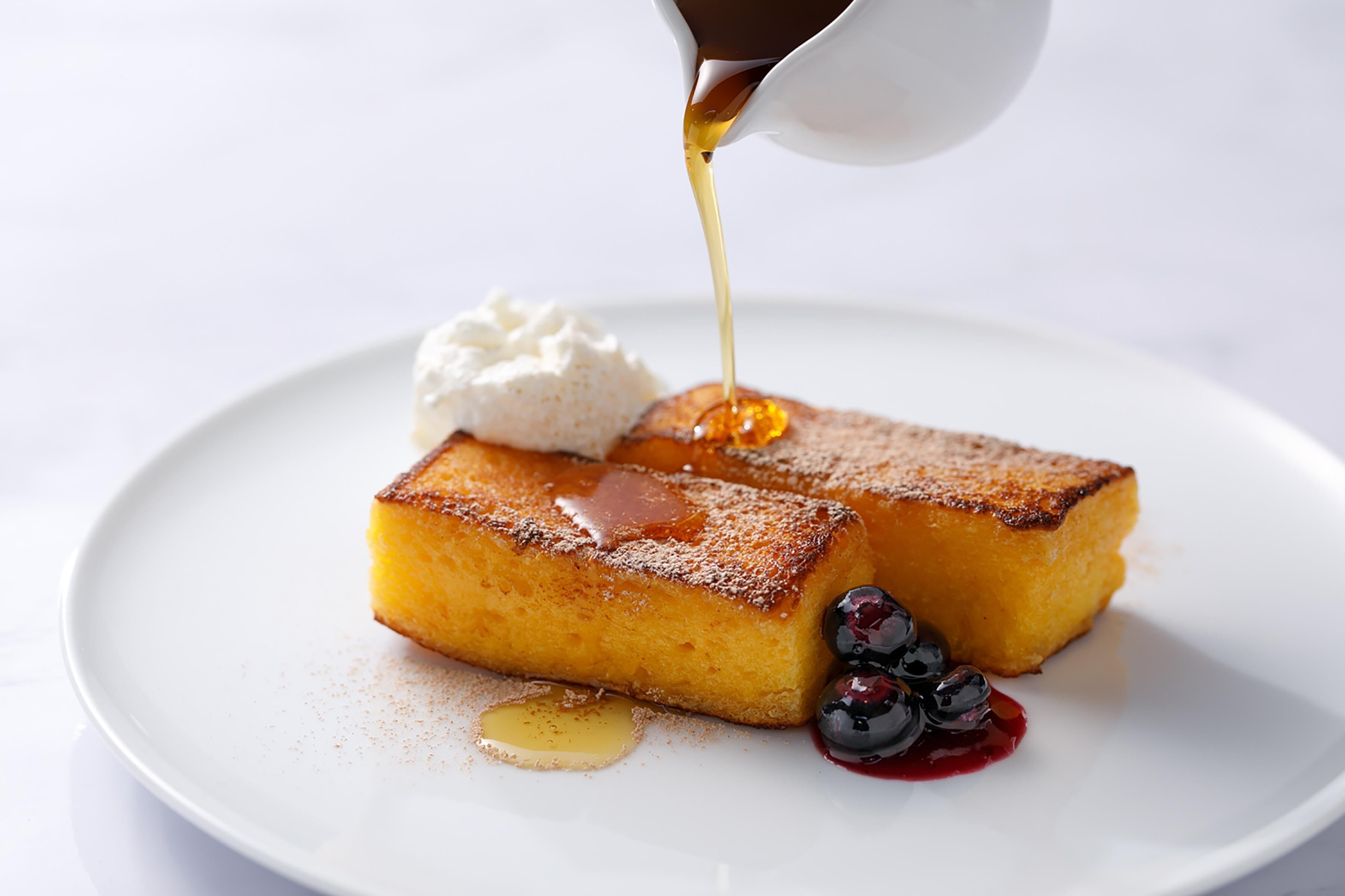 Une assiette de dessert avec un gâteau à la crème pâtissière, de la crème fouettée et des fruits rouges, le tout nappé de sirop.