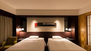Quarto de hotel com duas camas, uma escrivaninha, uma cadeira e uma obra de arte na parede.