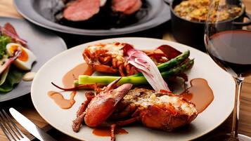 A lobster dish on a plate with asparagus and sauce, a fork, and a glass of red wine.