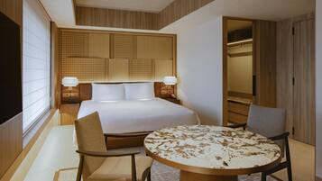 Quarto de hotel com uma cama grande, duas mesas de cabeceira com abajures, uma mesa de jantar redonda e uma cadeira.