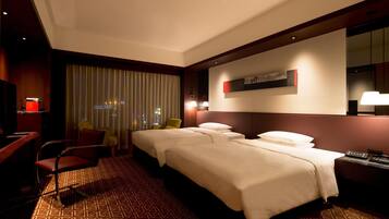 A hotel room with two beds, a desk, a chair, a TV, and a window with curtains.