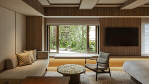 Een moderne hotelkamer met een bank, fauteuil, rond bijzettafeltje en een groot televisiescherm.