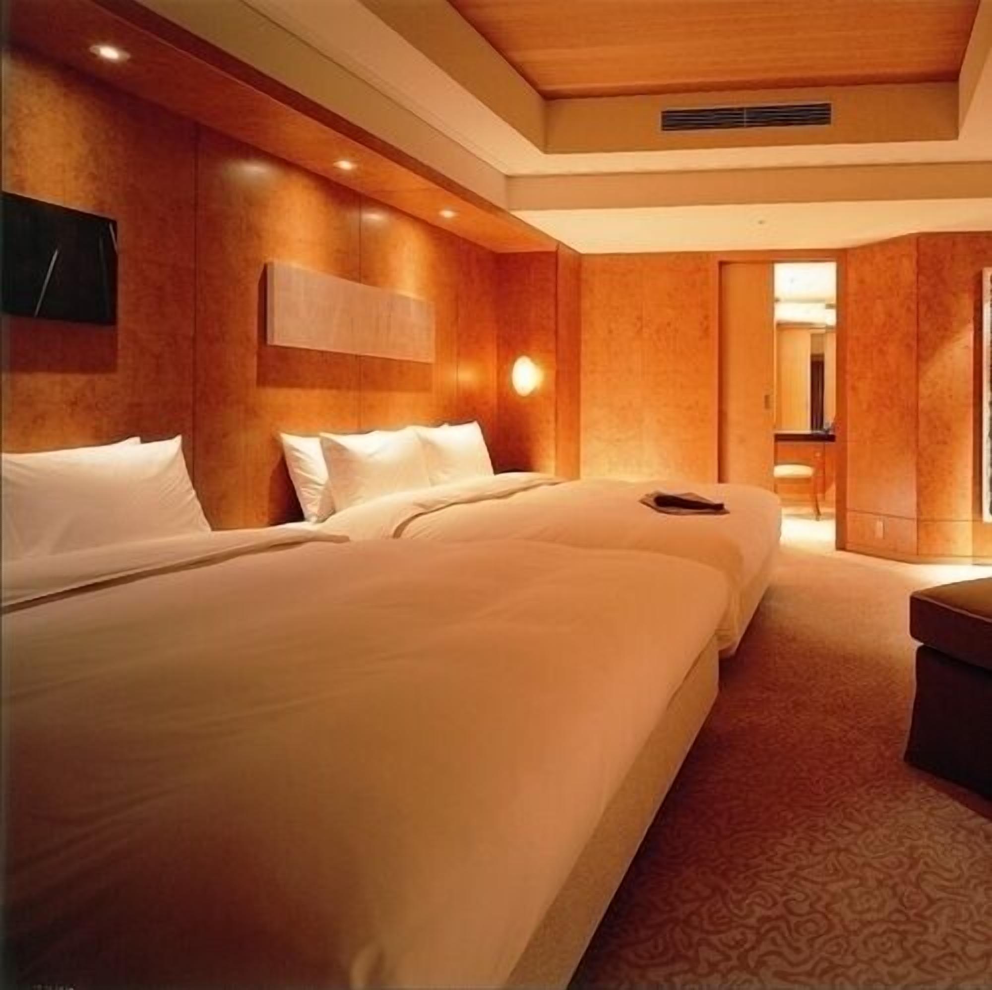 Een hotelkamer met twee bedden, een houten hoofdbord, een wandlamp en een deur naar een andere kamer.