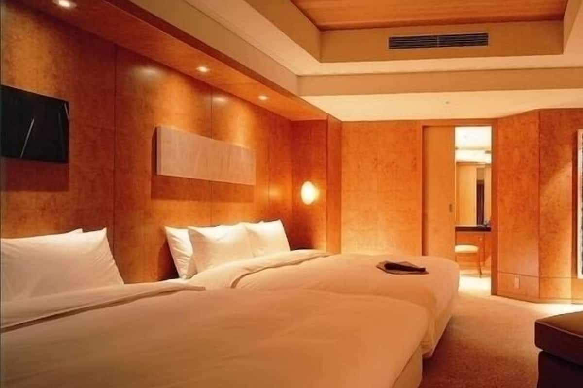 A hotel room with two beds, a wooden headboard, a wall-mounted light, and a door leading to another room.
