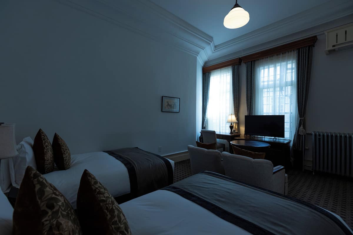 Una habitación de hotel con dos camas, un escritorio con televisor y una ventana con cortinas.