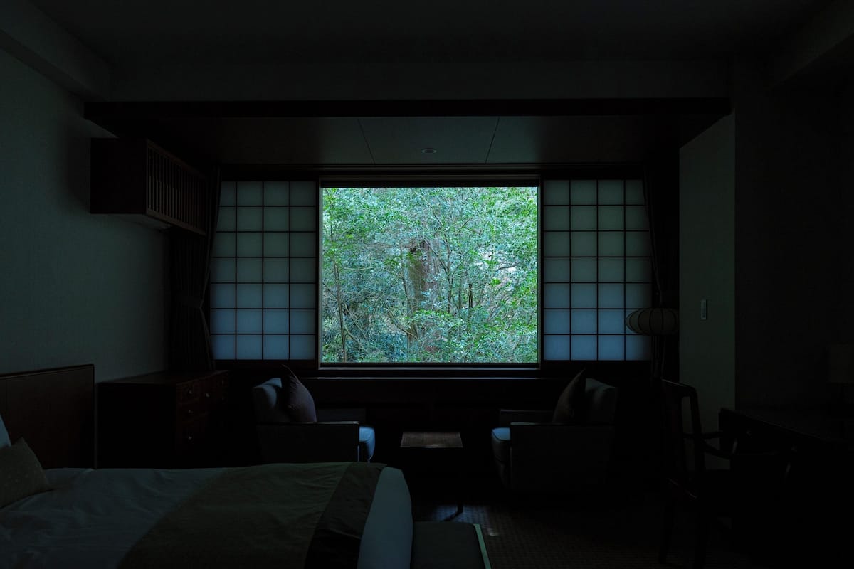 Una habitación tenuemente iluminada con un ventanal grande, una cama y un escritorio.