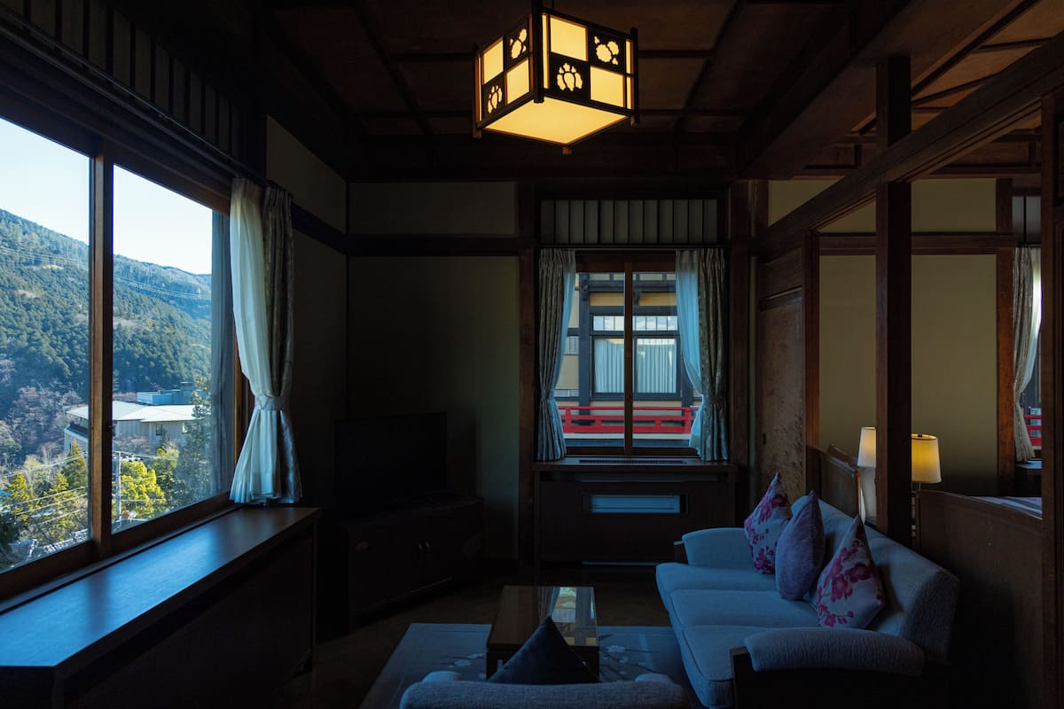 Una habitación tradicional japonesa con suelo de tatami, una mesa de madera baja, un sofá con cojines y un televisor sobre un mueble bajo.