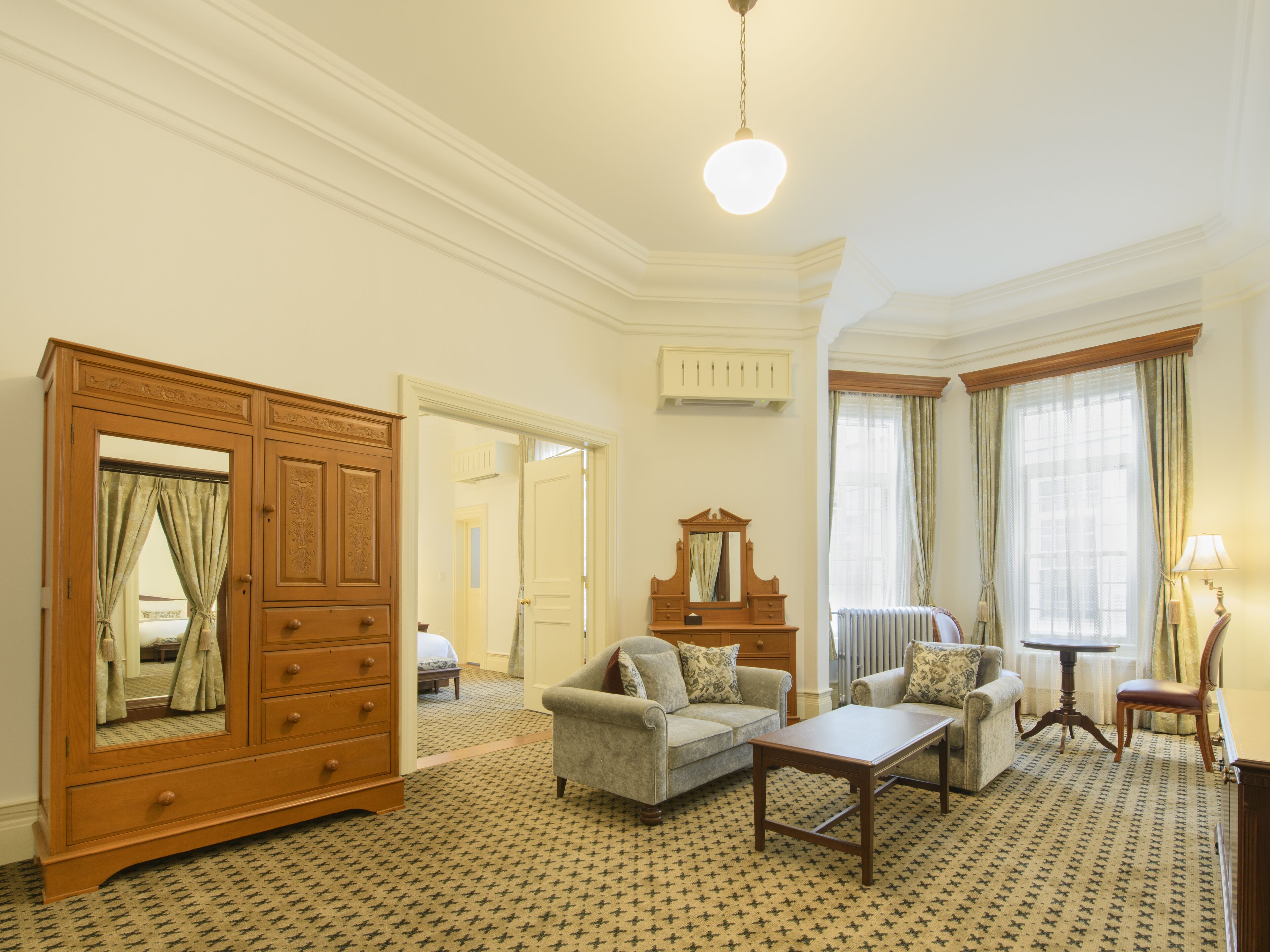 Une chambre d’hôtel avec une grande armoire en bois, deux fauteuils, une petite table et un miroir.