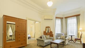 Une chambre d’hôtel avec une grande armoire en bois, deux fauteuils, une petite table et un miroir.