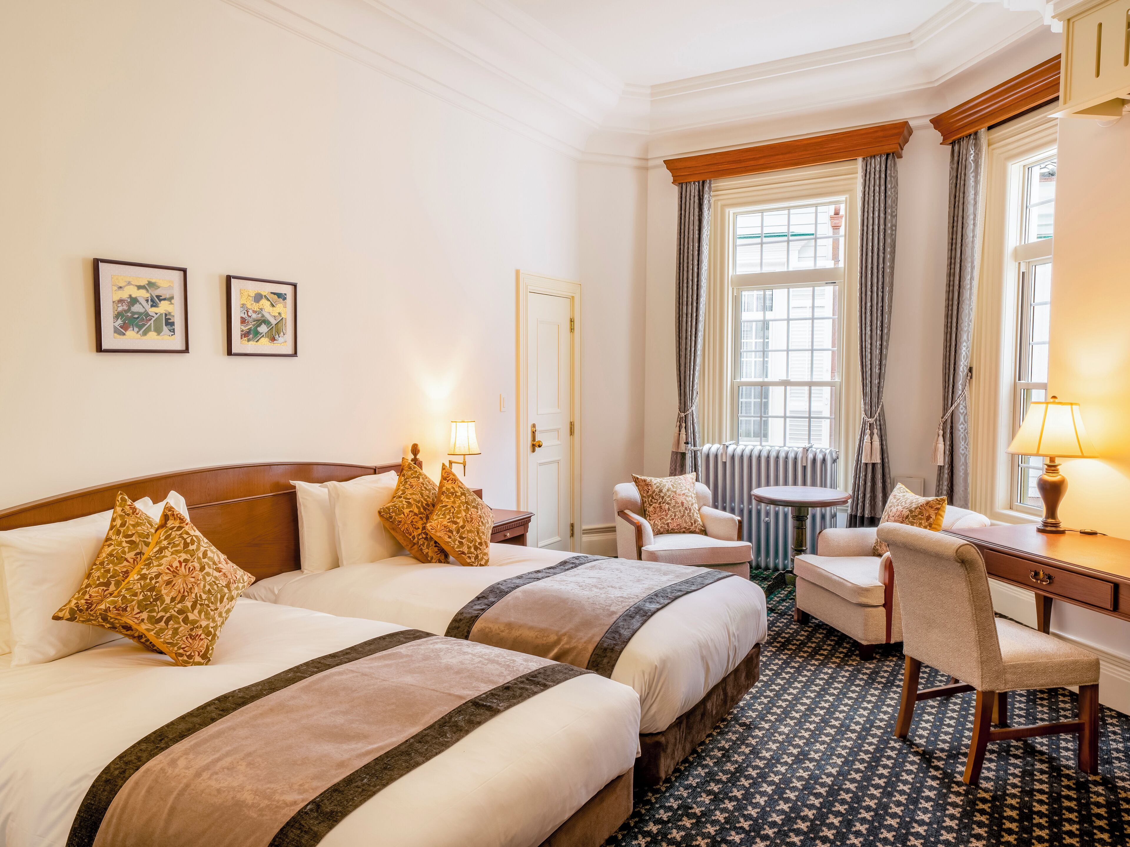 A hotel room with two beds, a chair, a table, and a window with curtains.
