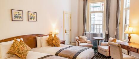 Une chambre d’hôtel avec deux lits, une chaise, une table et une fenêtre avec des rideaux.