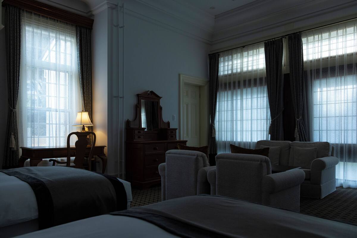 Habitación de hotel con una cama grande, dos sillones, un escritorio con lámpara, un aparador y un espejo.