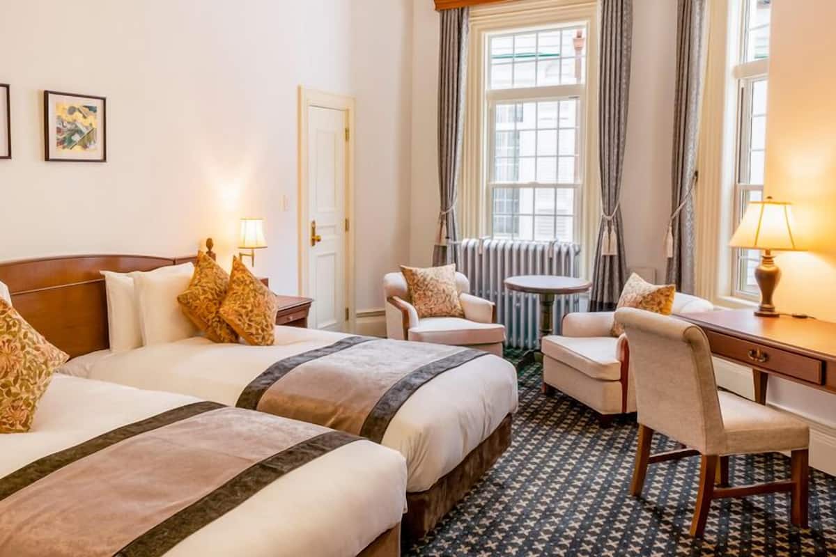 Habitación de hotel con dos camas, un escritorio, una silla, una mesa y dos cuadros en la pared.