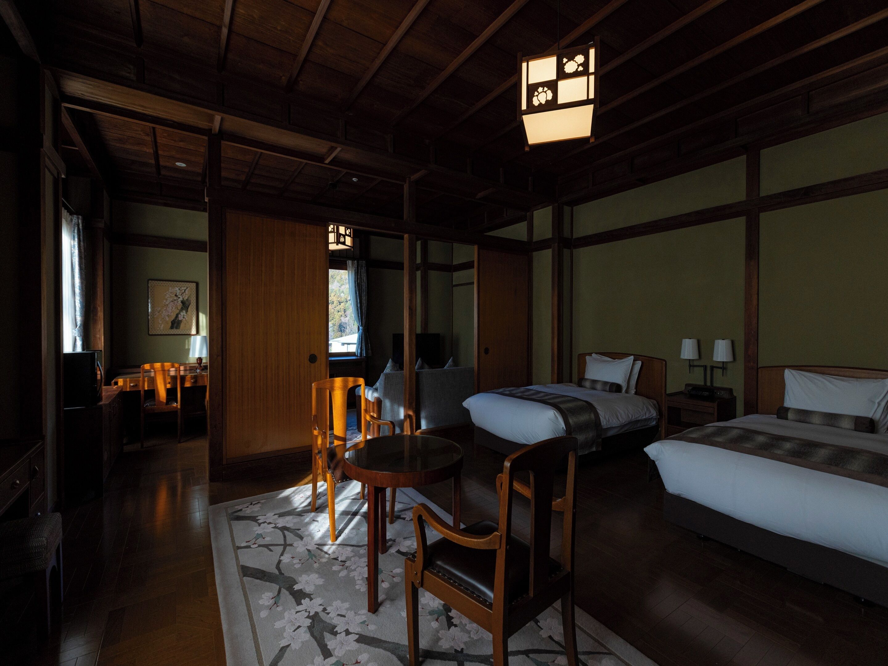 Una camera tradizionale in stile giapponese con soffitto in legno, pavimento in tatami, un letto, una scrivania e una sedia.