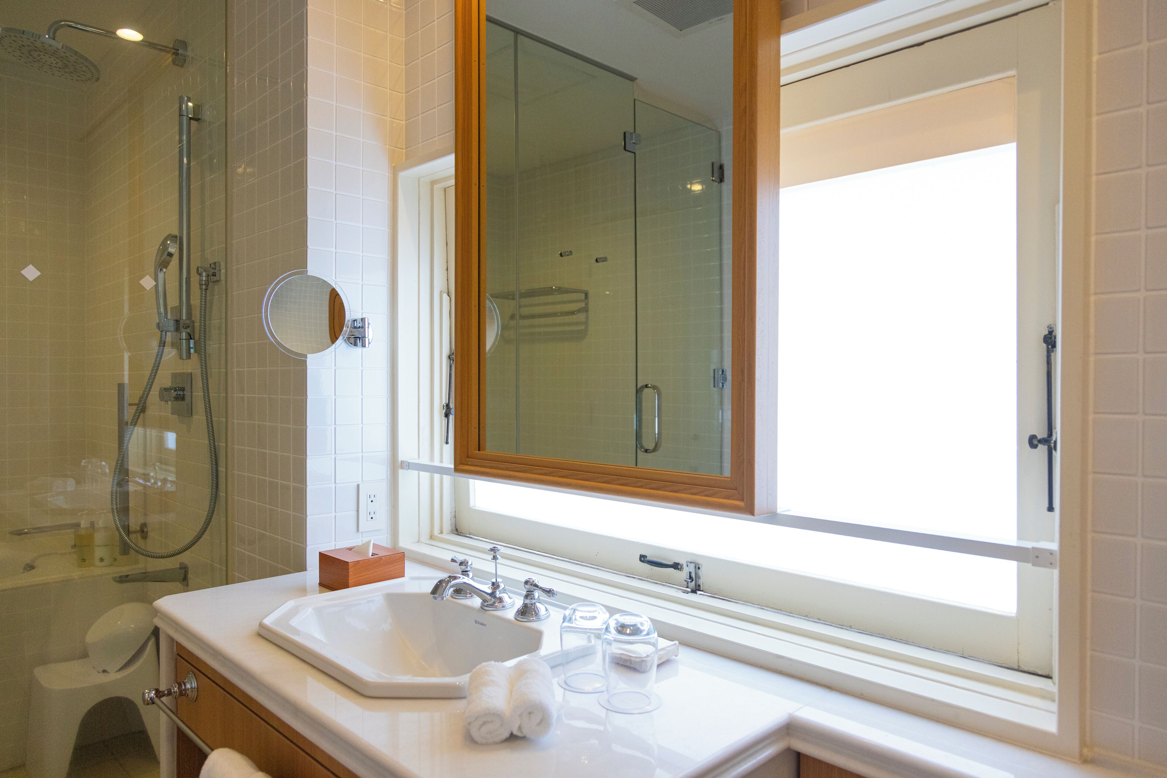 Un baño moderno con cabina de ducha de vidrio, un lavamanos con espejo y una ventana que proporciona luz natural.