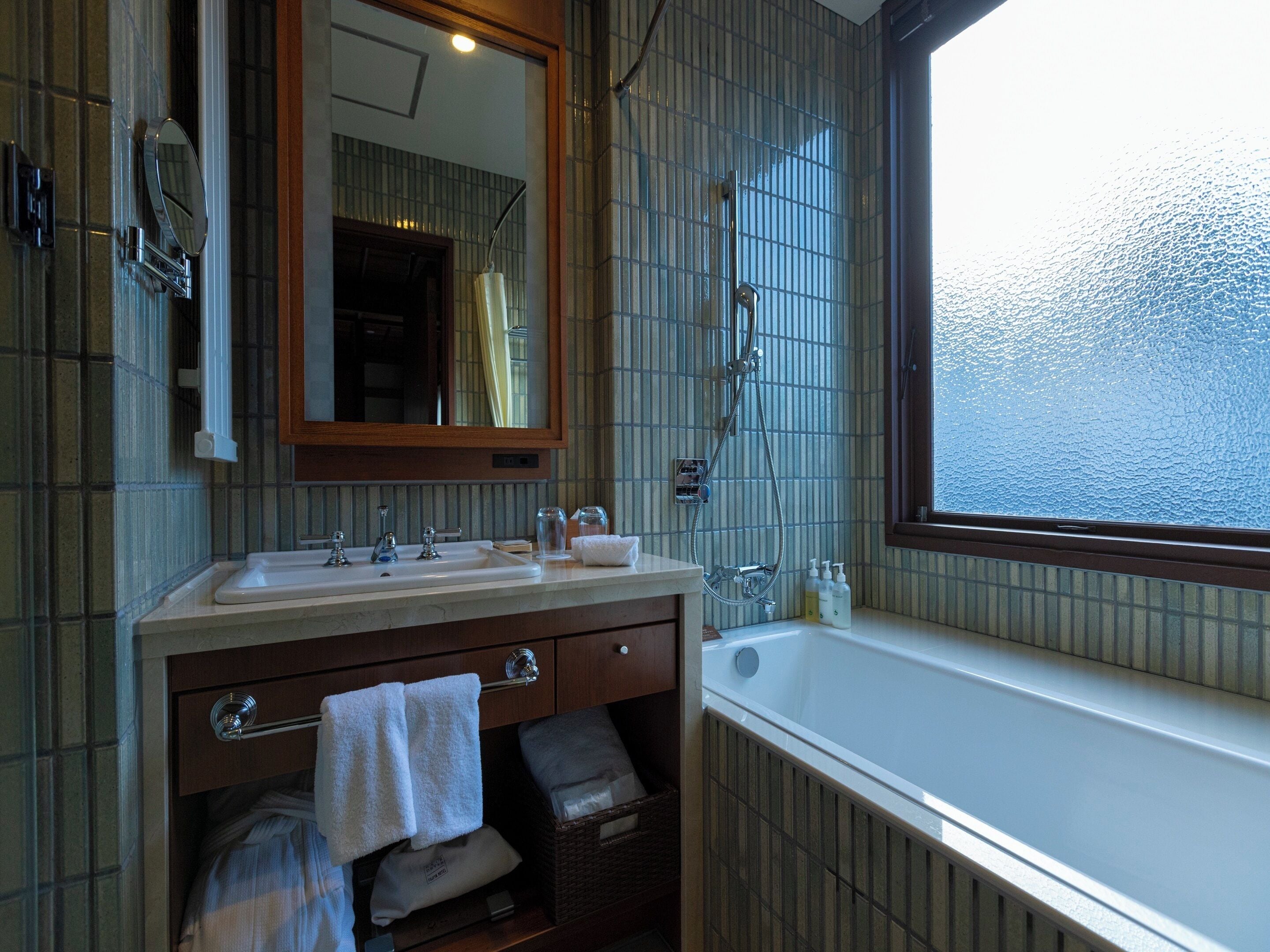 A bathroom with a bathtub, two sinks, a mirror, and a window.