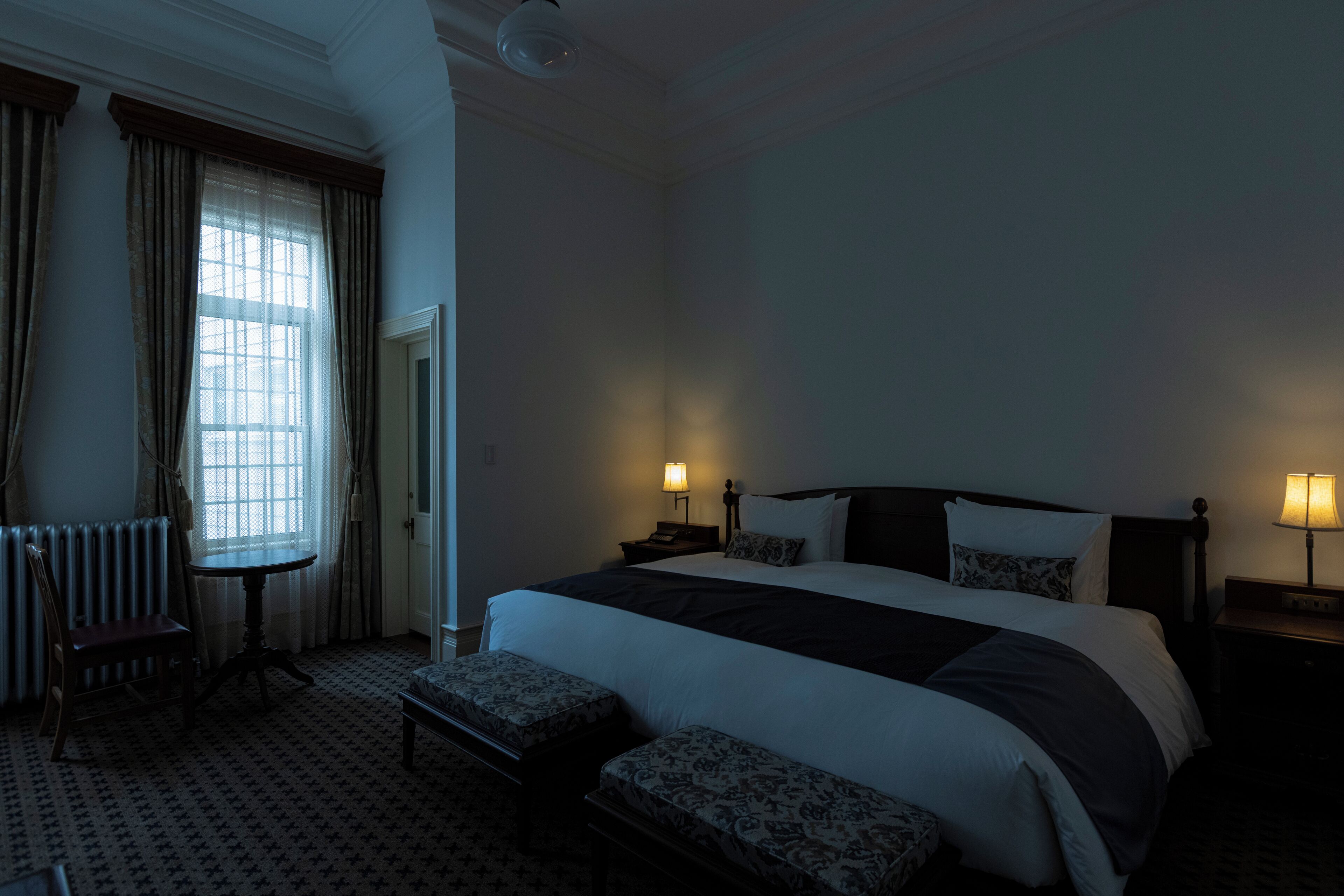 A hotel room with a large bed, two bedside tables with lamps, a chair, and a small table.