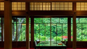 Una habitación japonesa tradicional con suelo de esteras de tatami, una mesa baja y vistas a un follaje exuberante a través de amplias ventanas.