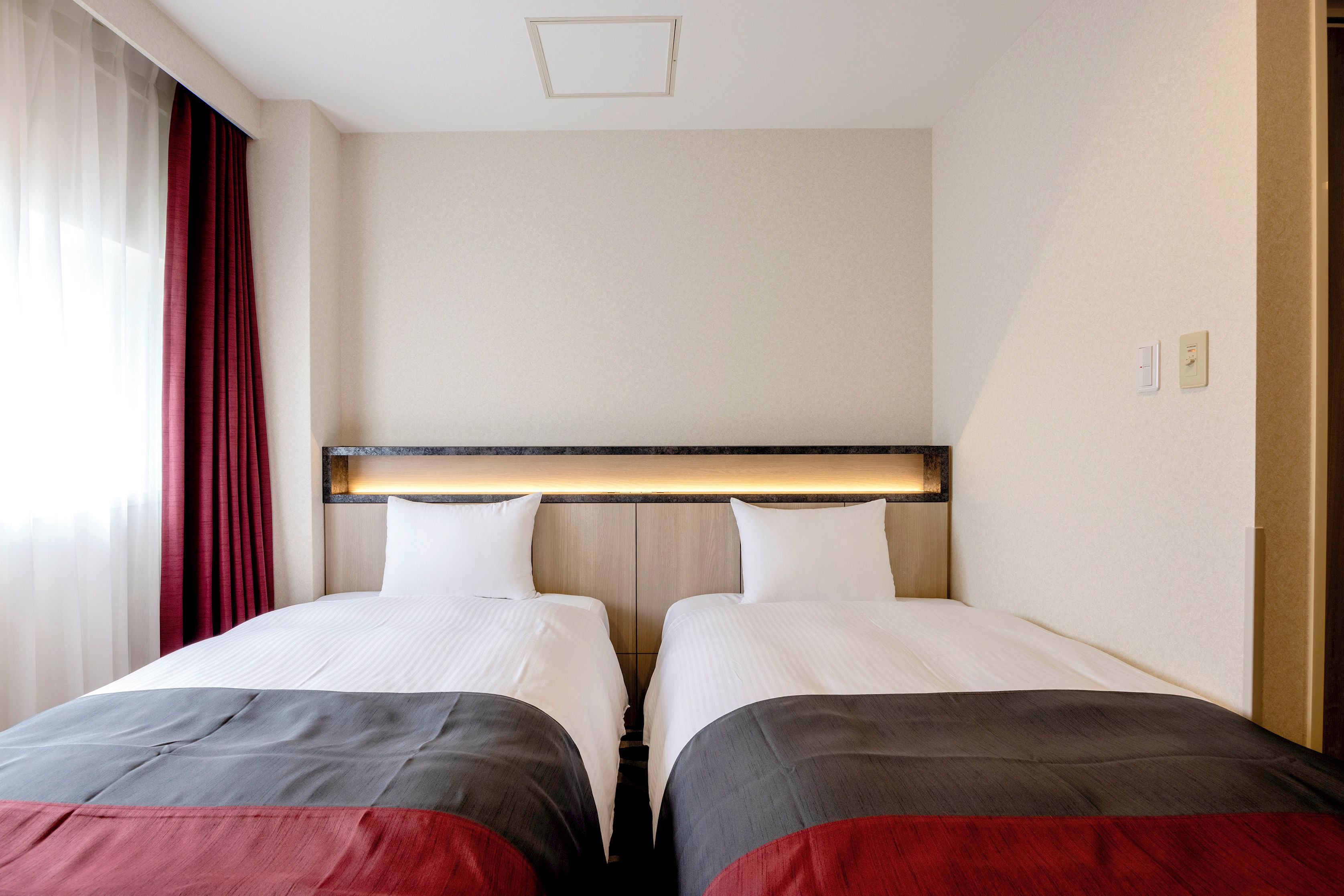 A hotel room with two beds, a wooden headboard, a light switch, and a power outlet on the wall.