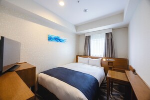 A hotel room with a bed, a desk, a television, and a window with curtains.